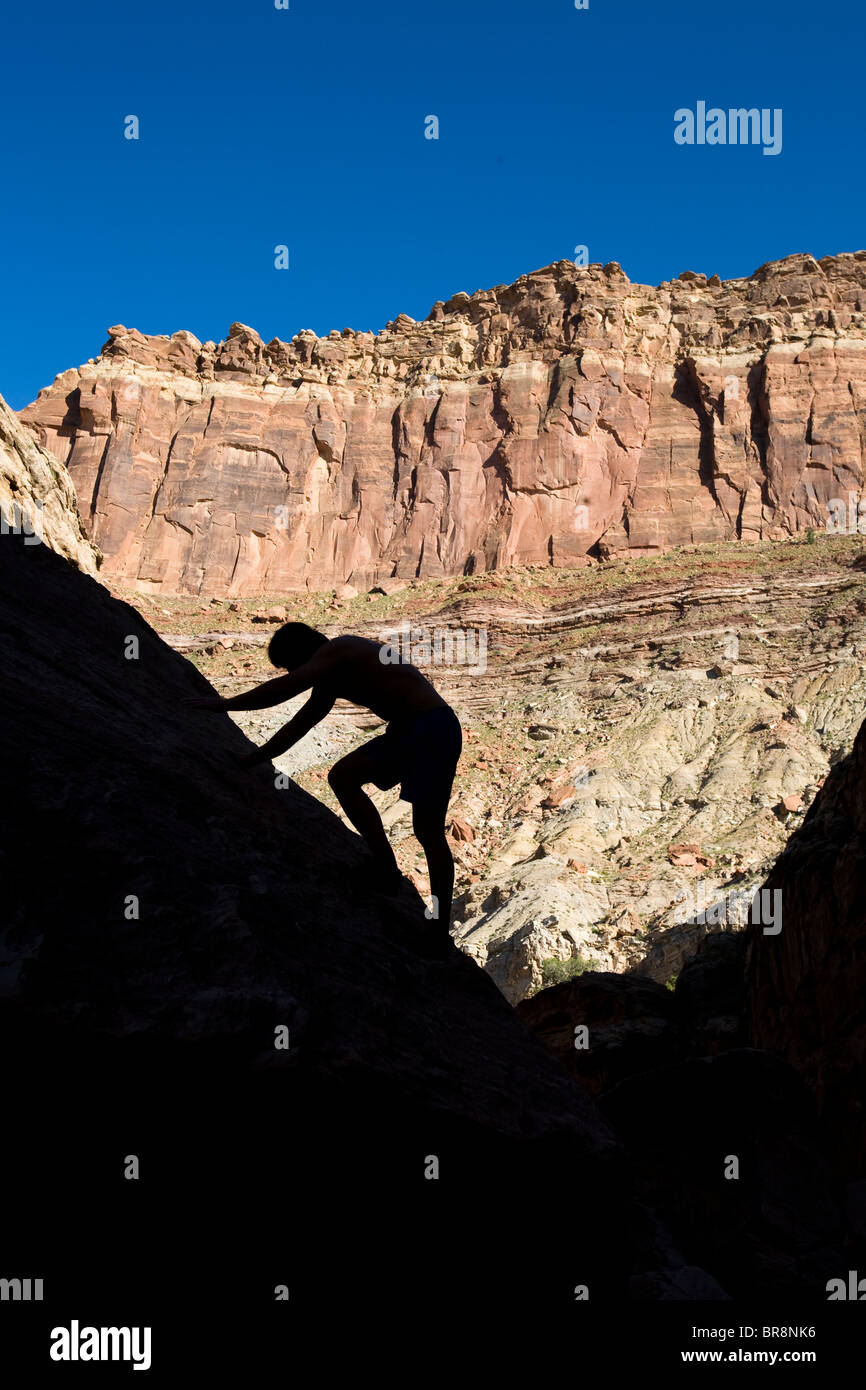 A silhouetted man scrambles up a rock wall in Eardley Canyon San Rafael Swell Utah. Stock Photo
