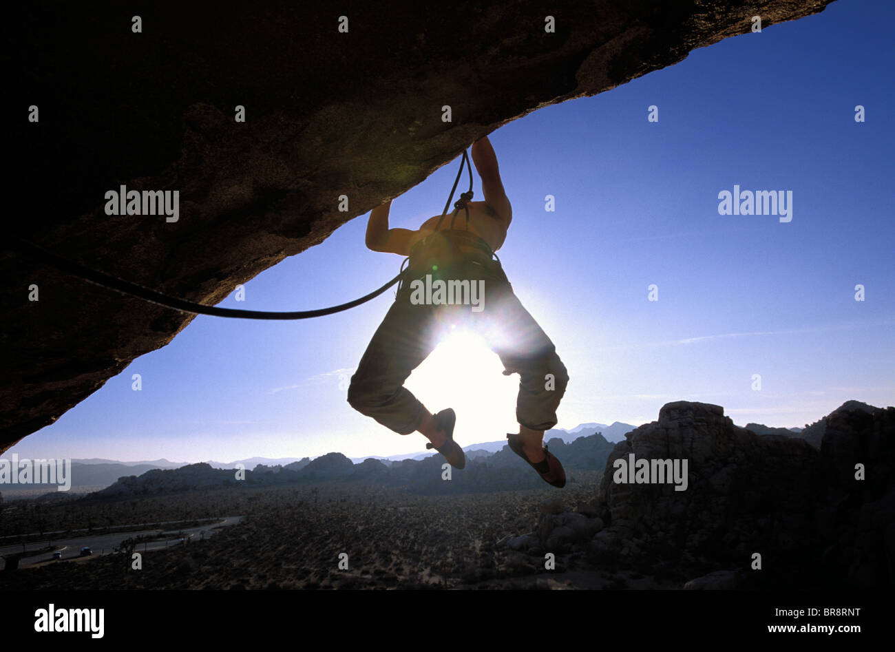 Silhouette of a man climbing and hanging from an overhang Stock Photo
