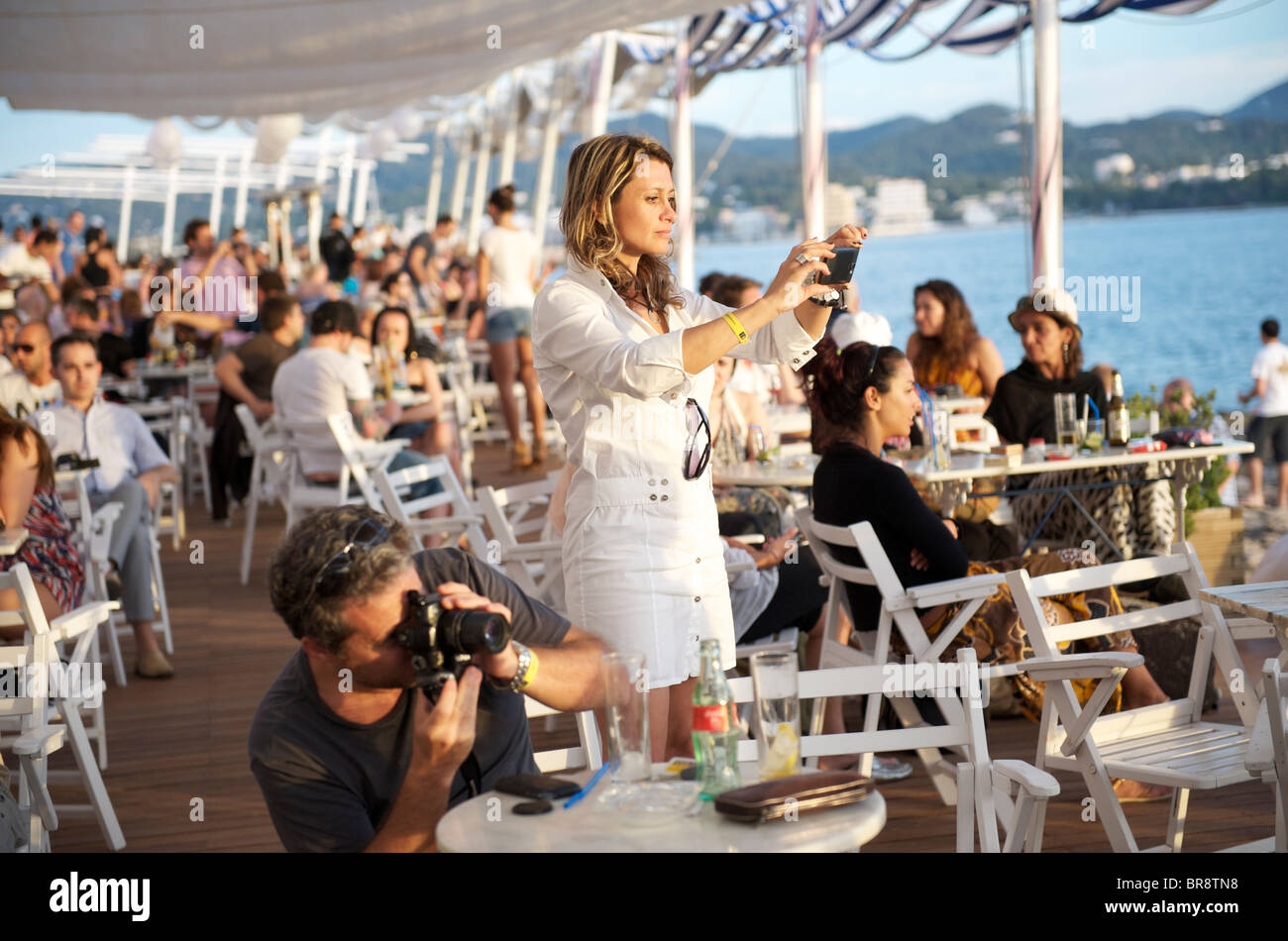 tourists taking a photograph of the sunset at cafe del mar in ibiza with an iphone and camera Stock Photo