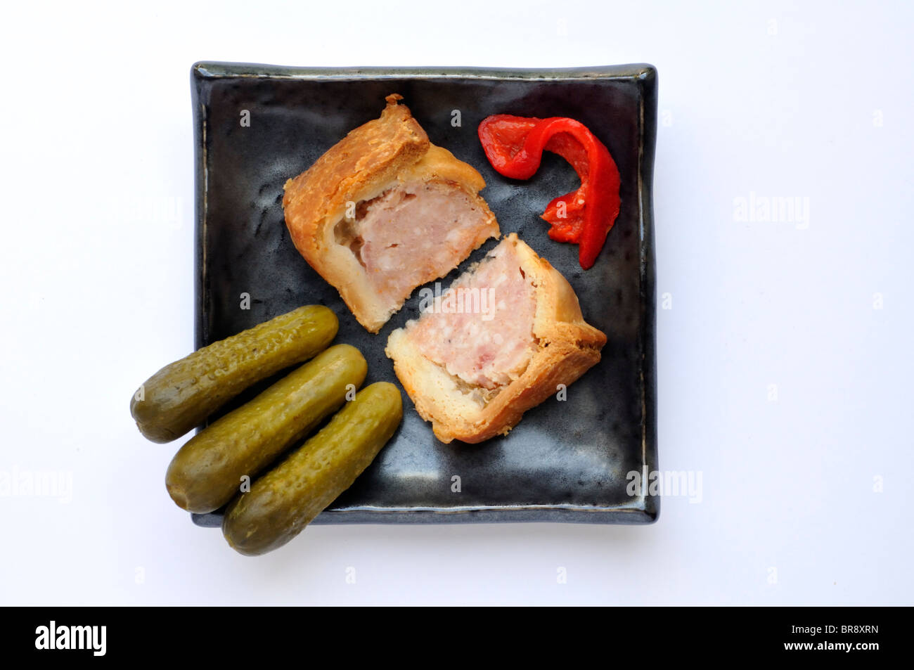 Two wedges of common British pork pie with miniature gherkins and roasted red peppers. Stock Photo