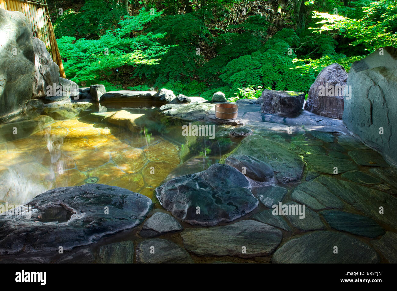 Rotenburo, outdoor onsen, facing green foliage and next to a clear mountain stream Stock Photo