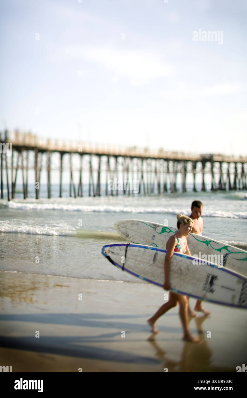 Two people walking on the beach with surfboards Oceanside CA Stock