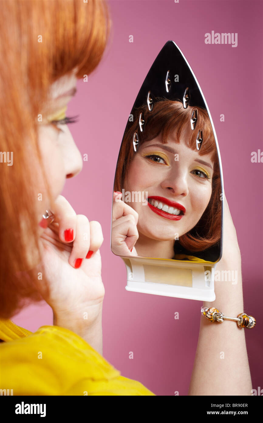 portrait of redhead woman looking at her reflection in iron and checking in her make-up Stock Photo