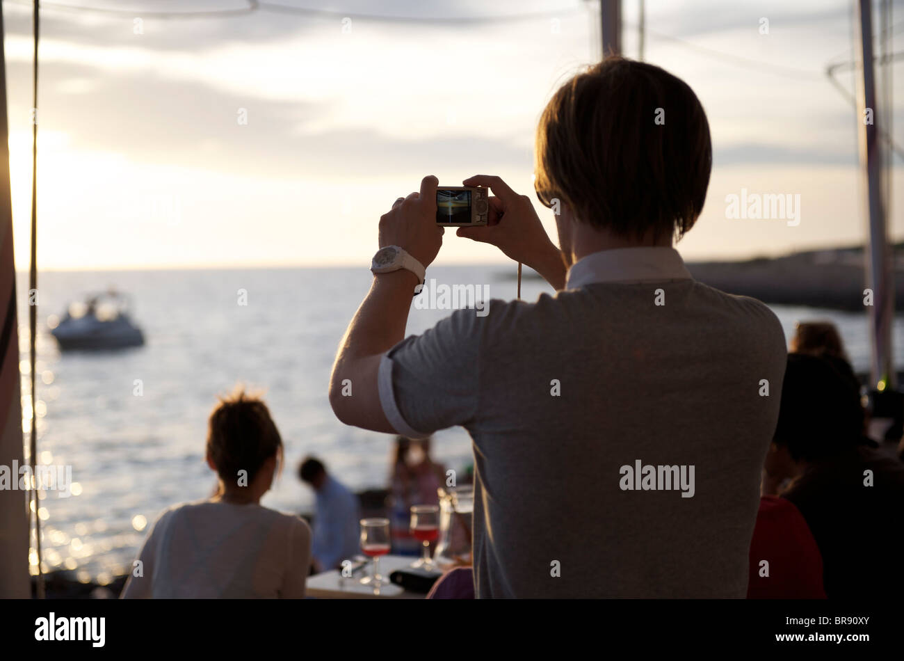 young man taking a photograph of the sunset at cafe del mar in ibiza , spain Stock Photo