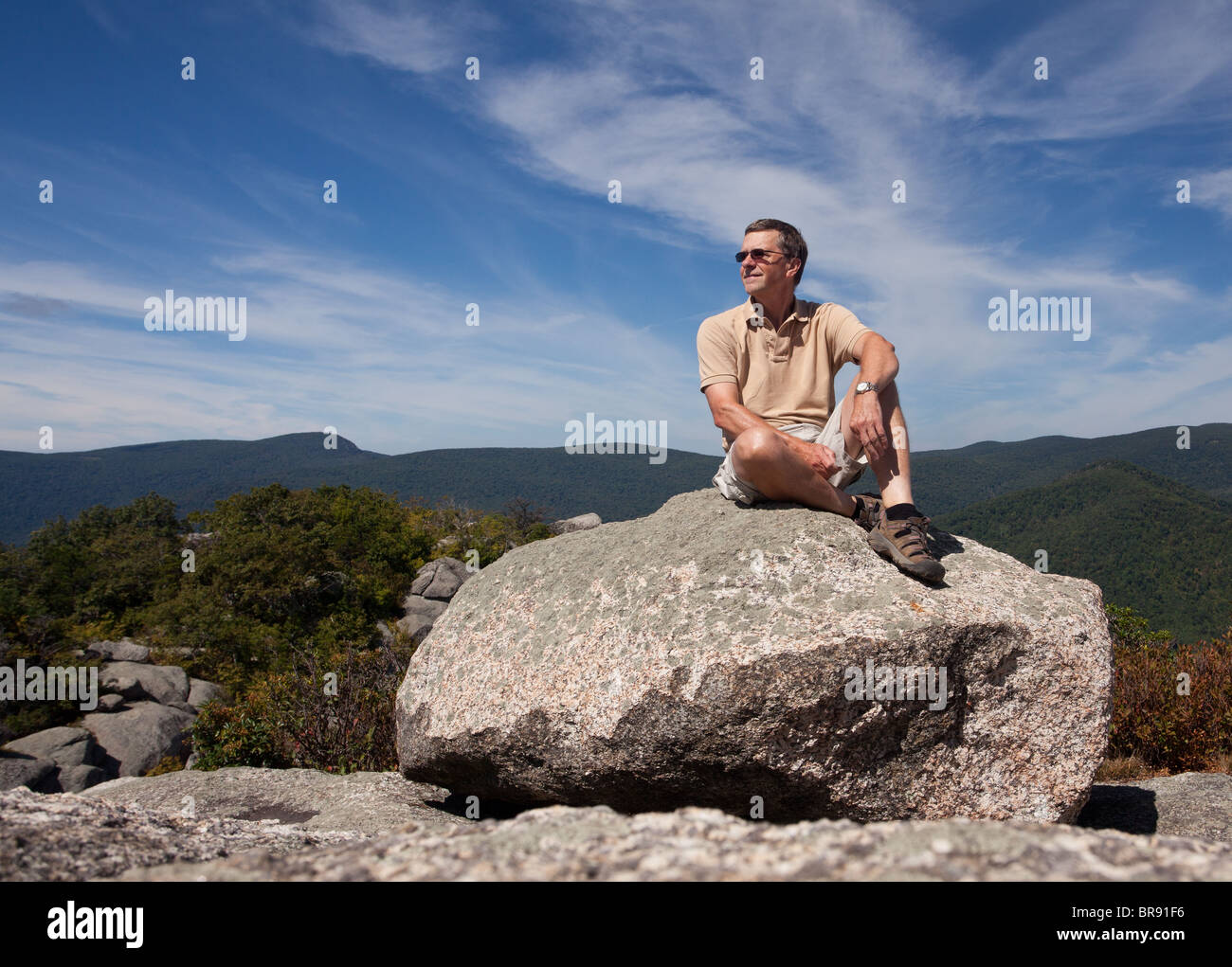 Middle aged hiker on large boulder at the summit of Old Rag in Virginia's Shenandoah valley in the Blue Ridge Mountains, USA Stock Photo