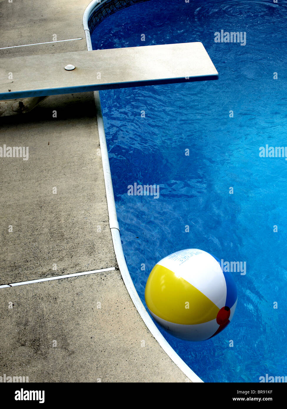 edge of home inground swimming pool with blue water cement deck diving board and beach ball