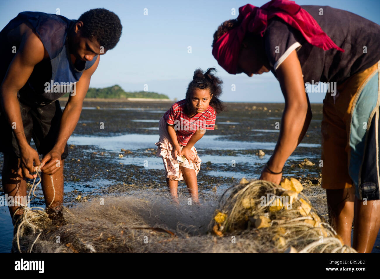 Two young girls and a young man wrap up a fishing net after fishing during low tide. Stock Photo