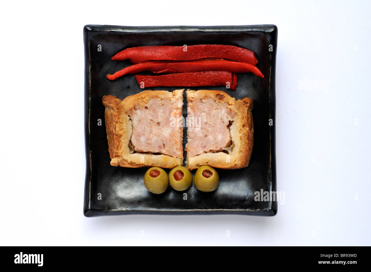 Two wedges of common British pork pie with roasted red peppers and pimiento stuffed olives. Stock Photo