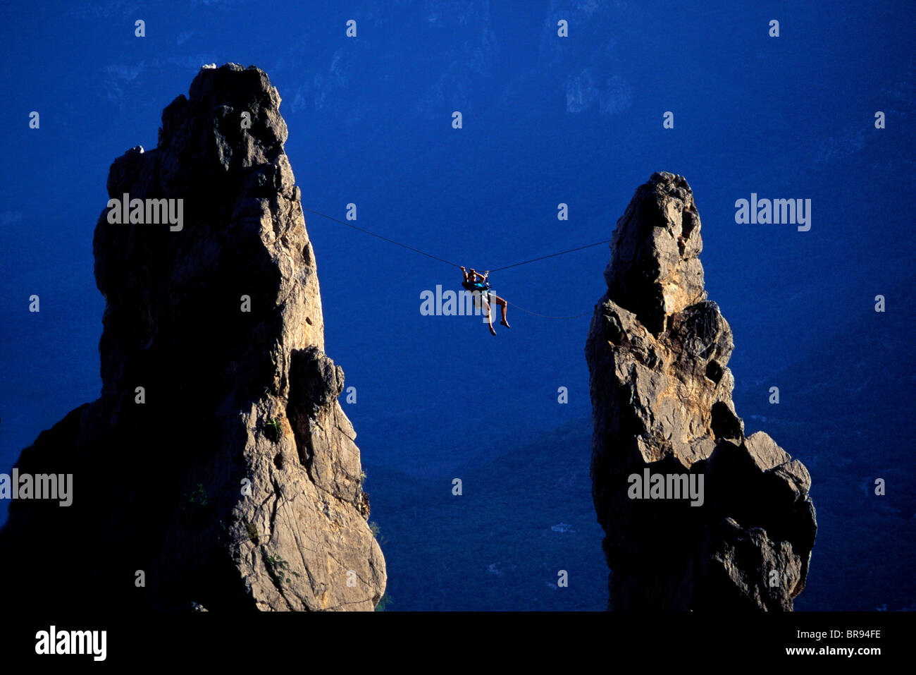 Man doing a Tyrolean Traverse between two spires while climbing. Stock Photo