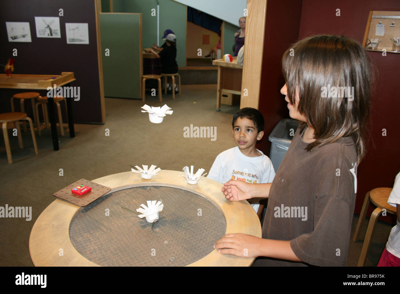 Two children experimenting with hand made paper creations and wind machine, looking at flight, hover craft, aerodynamics. Stock Photo