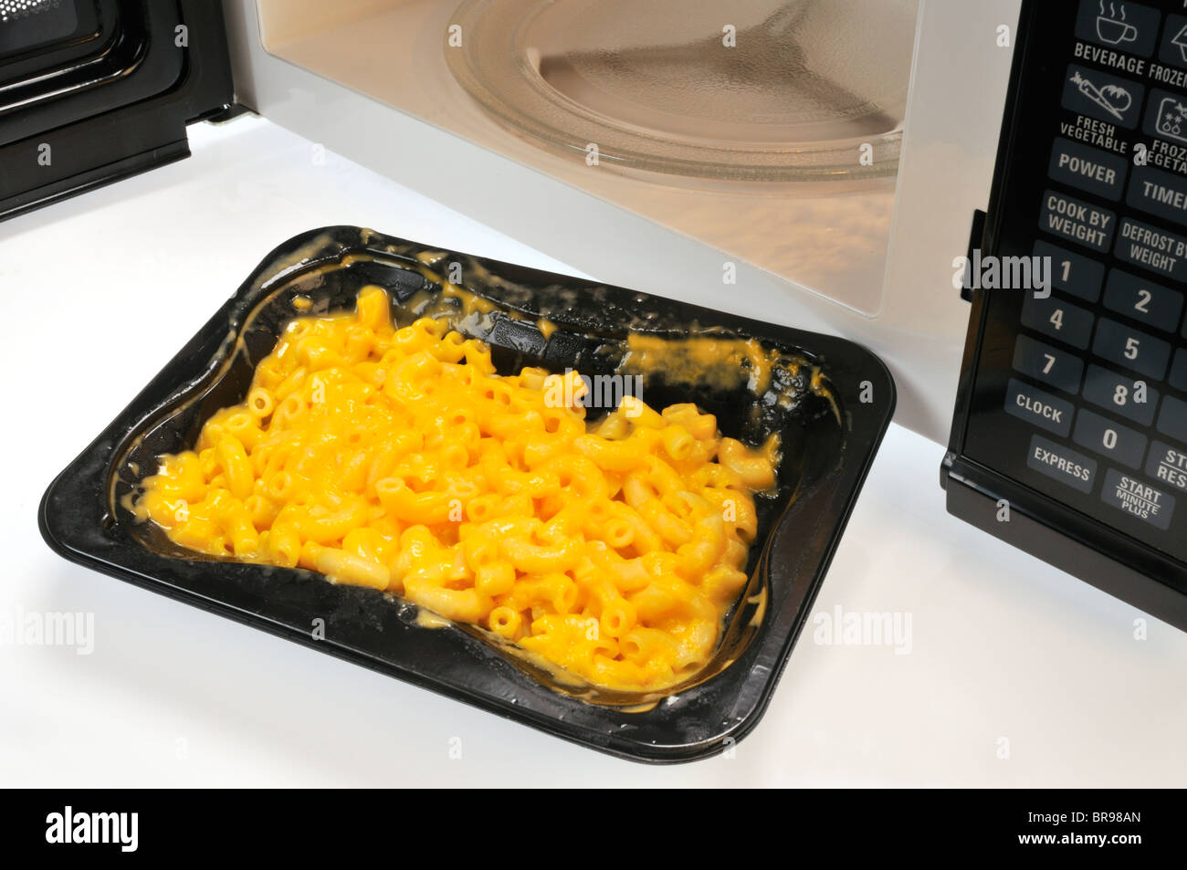 Tray of cooked macaroni pasta and cheese in front of microwave with door open Stock Photo