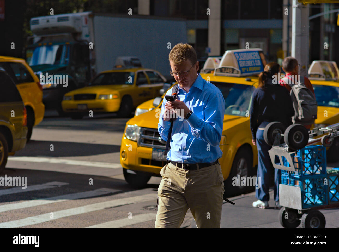 Man in blue shirt crossing busy street while operating hand-held device. Stock Photo