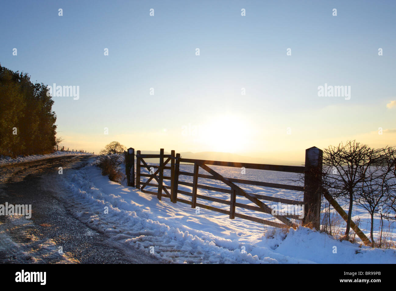 Backlit farm gate during winter with snow on the ground Stock Photo