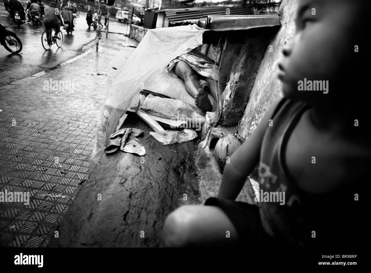 Son watches bypassers waiting for mother to wake in Hanoi Vietnam. Stock Photo
