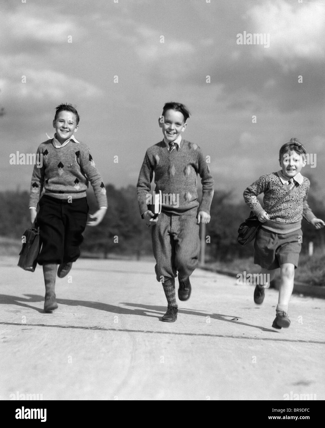 1930s THREE BOYS RUNNING CARRYING SCHOOL BOOKS Stock Photo