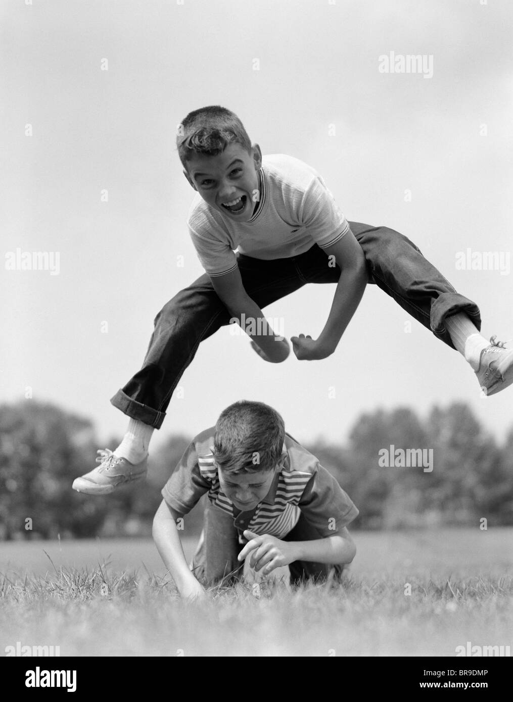1960s BOYS PLAYING LEAP FROG OUTSIDE SKY GRASS JUMP JUMPING CROUCHING Stock Photo