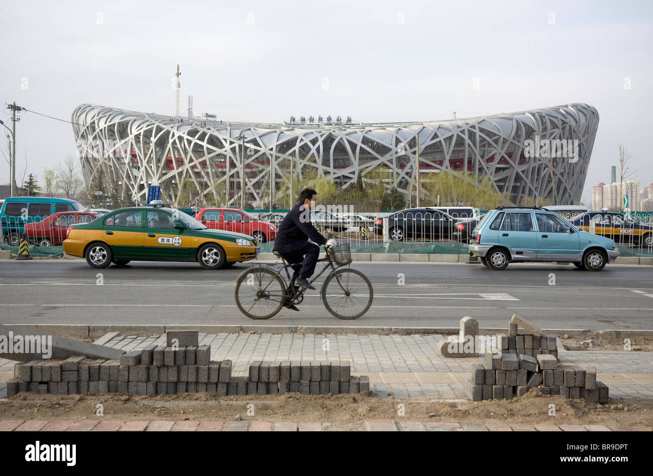A cyclist and other vehicles pass the newly constructed Bird's Nest Stadium Beijing China. Stock Photo