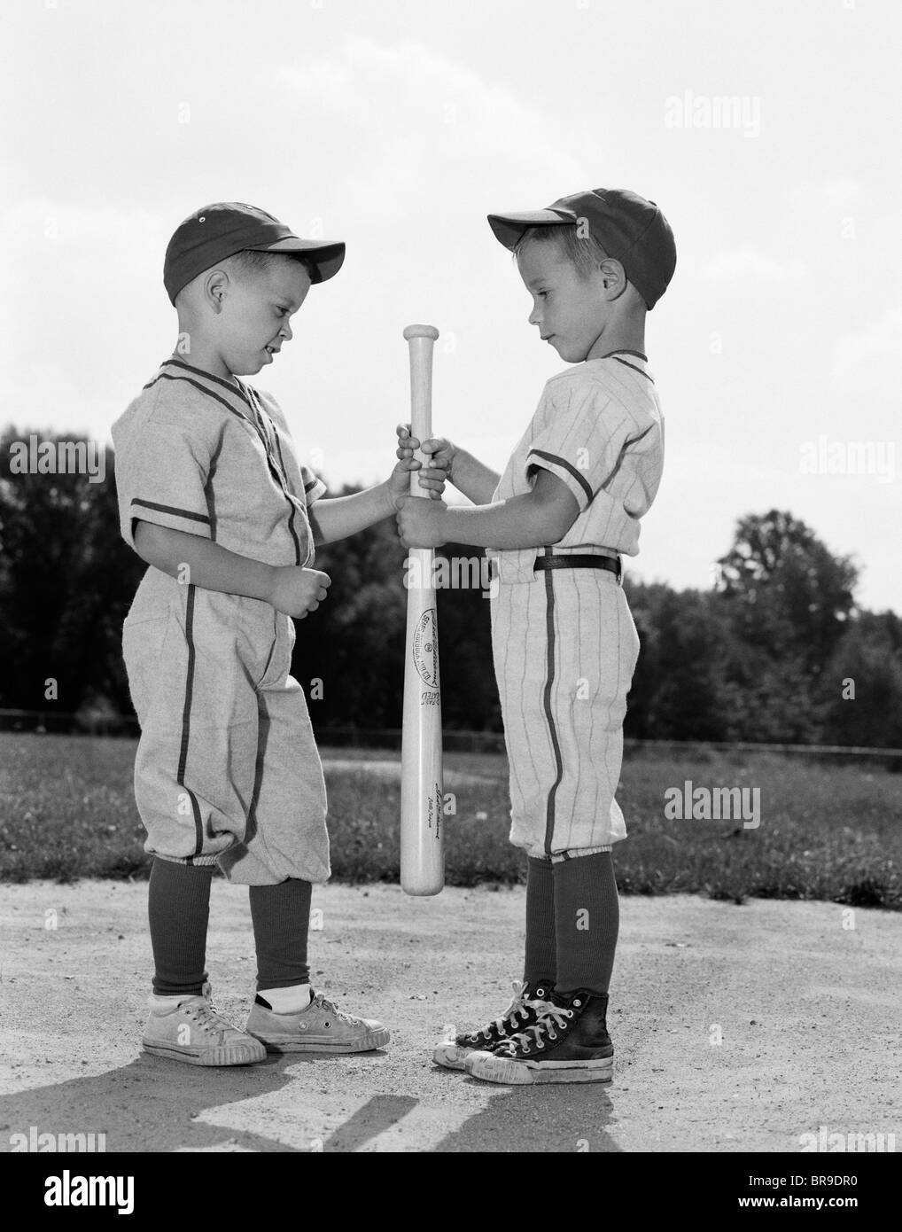 1960s TWO BOYS IN BASEBALL UNIFORMS CHOOSING SIDES BY GETTING THE UPPER HAND ON A BAT Stock Photo