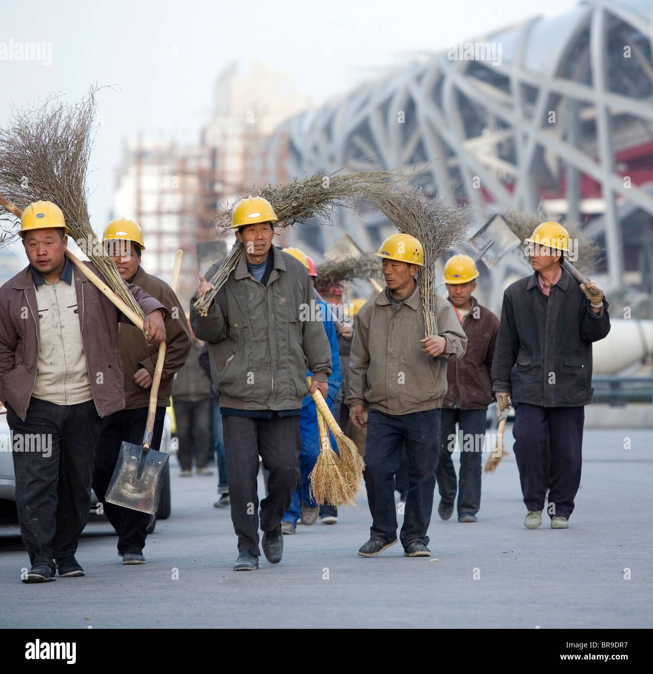 Migrant workers walk past the Bird's Nest Stadium as they make their way back to their dormitories after a day of laboring Beij Stock Photo