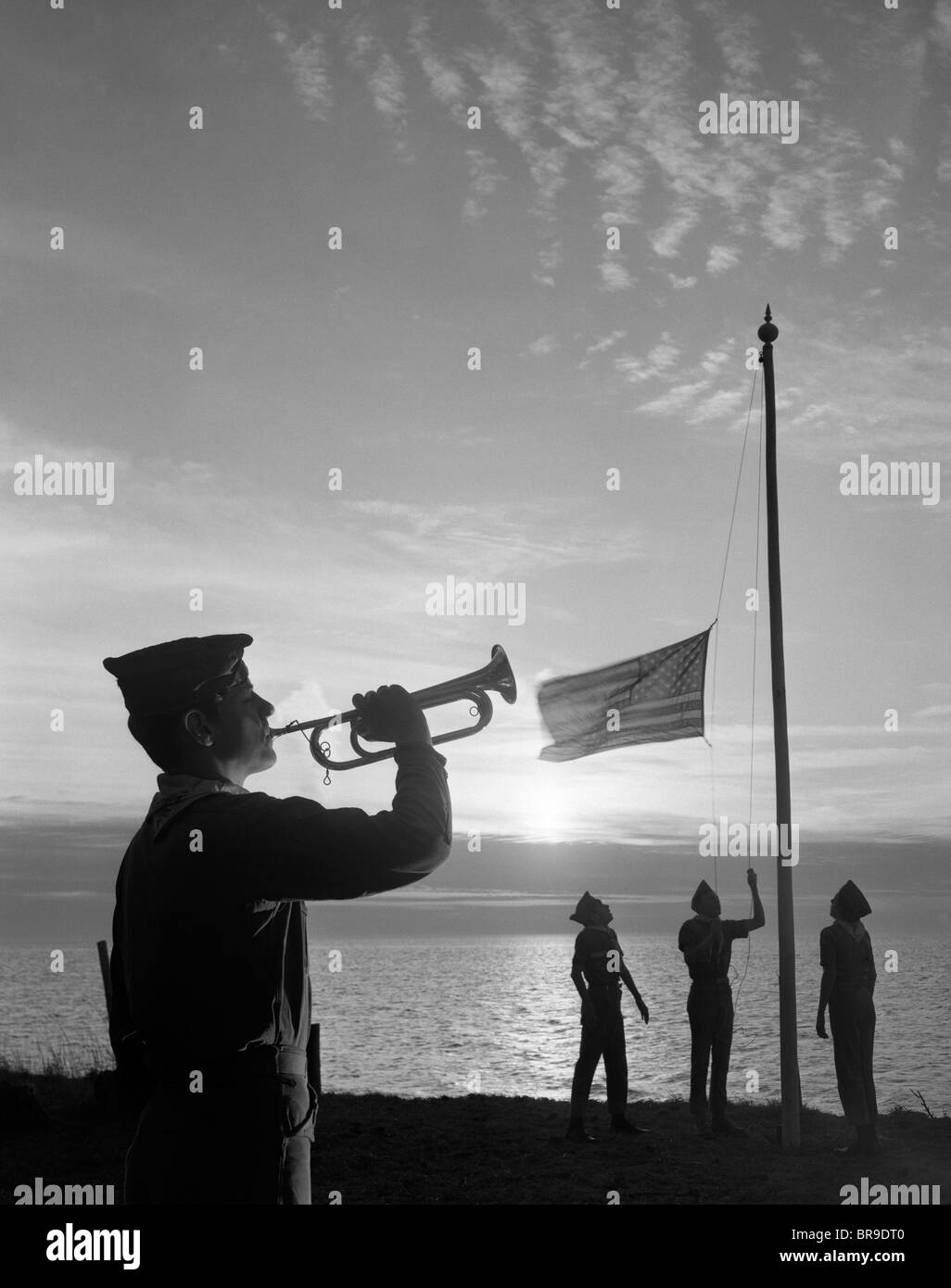 1960s BOY SCOUTS AT CAMP SUNSET LOWER AMERICAN FLAG BUGLE TAPS 4 BOYS UNIFORM SILHOUETTED Stock Photo