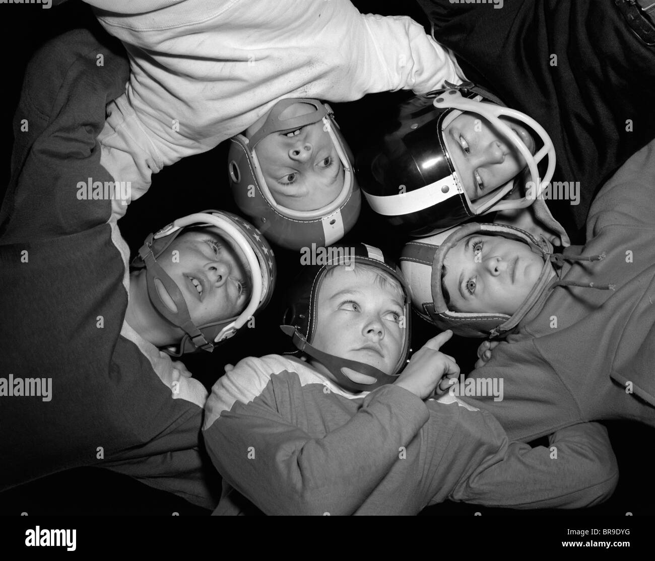 1960s FIVE BOYS IN HUDDLE WEARING HELMETS & FOOTBALL JERSEYS THE VIEW IS FROM INSIDE THE HUDDLE LOOKING UP Stock Photo