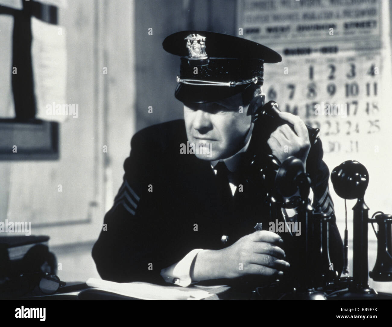 1930s 1940s CONCERNED DETERMINED MAN POLICE SERGEANT IN STATION HOUSE TALKING ON CANDLE STICK TELEPHONE Stock Photo