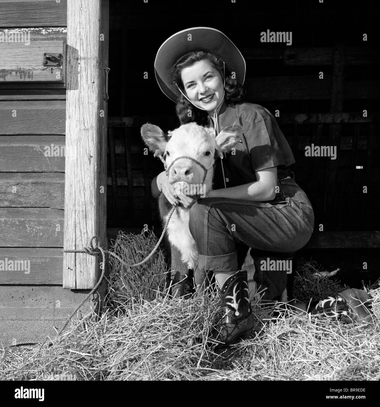 GIRL POSING WITH CALF IN STRAW FILLED STALL IN BARN Stock Photo
