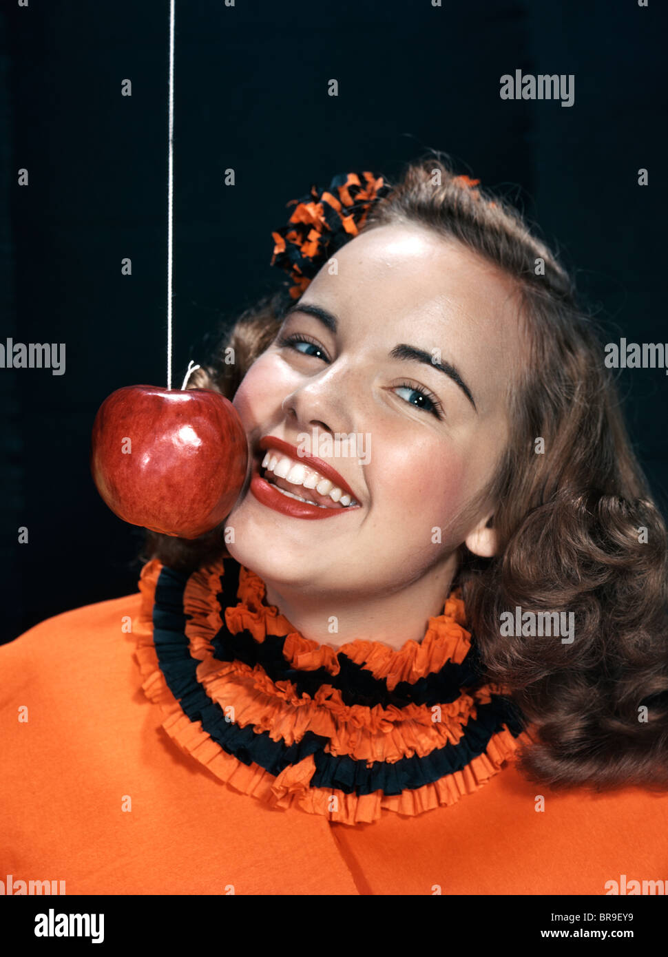 1940s 1950s SMILING YOUNG WOMAN WEARING HALLOWEEN COSTUME BOBBING FOR APPLE ON A STRING Stock Photo