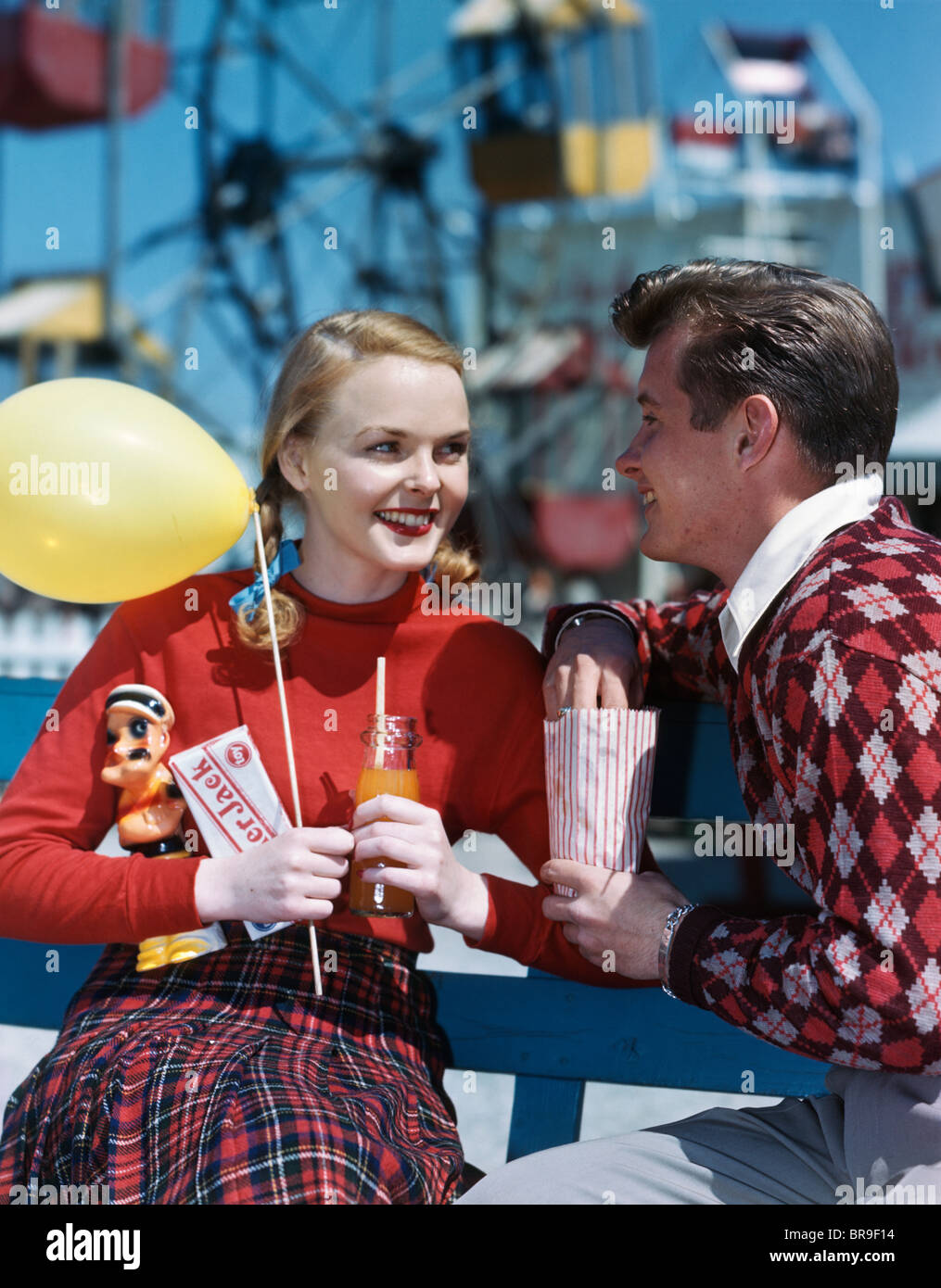 1940s 1950s YOUNG COUPLE AT AMUSEMENT PARK MAN EATING POPCORN WOMAN HOLDING BALLOON AND DRINK AND CRACKERJACK BOX Stock Photo