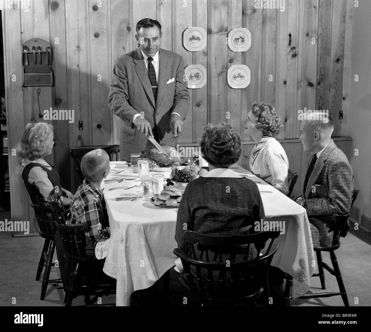 1950s FATHER STANDING AT DINNER TABLE KNOTTY PINE PANELED DINING ROOM READY TO SERVE FAMILY AND CARVE TURKEY Stock Photo