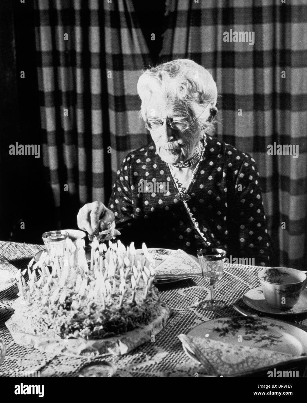 1940s 1950s ELDERLY SENIOR WOMAN ABOUT TO CUT BIRTHDAY CAKE COVERED IN CANDLES Stock Photo