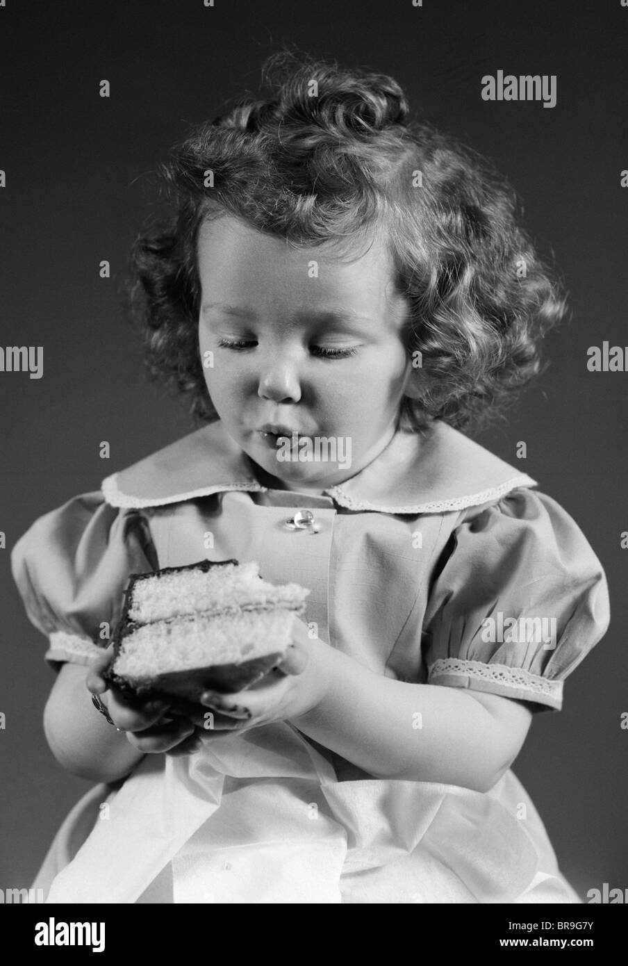 1940s LITTLE GIRL EATING PIECE OF CAKE WITH CHOCOLATE ICING Stock Photo