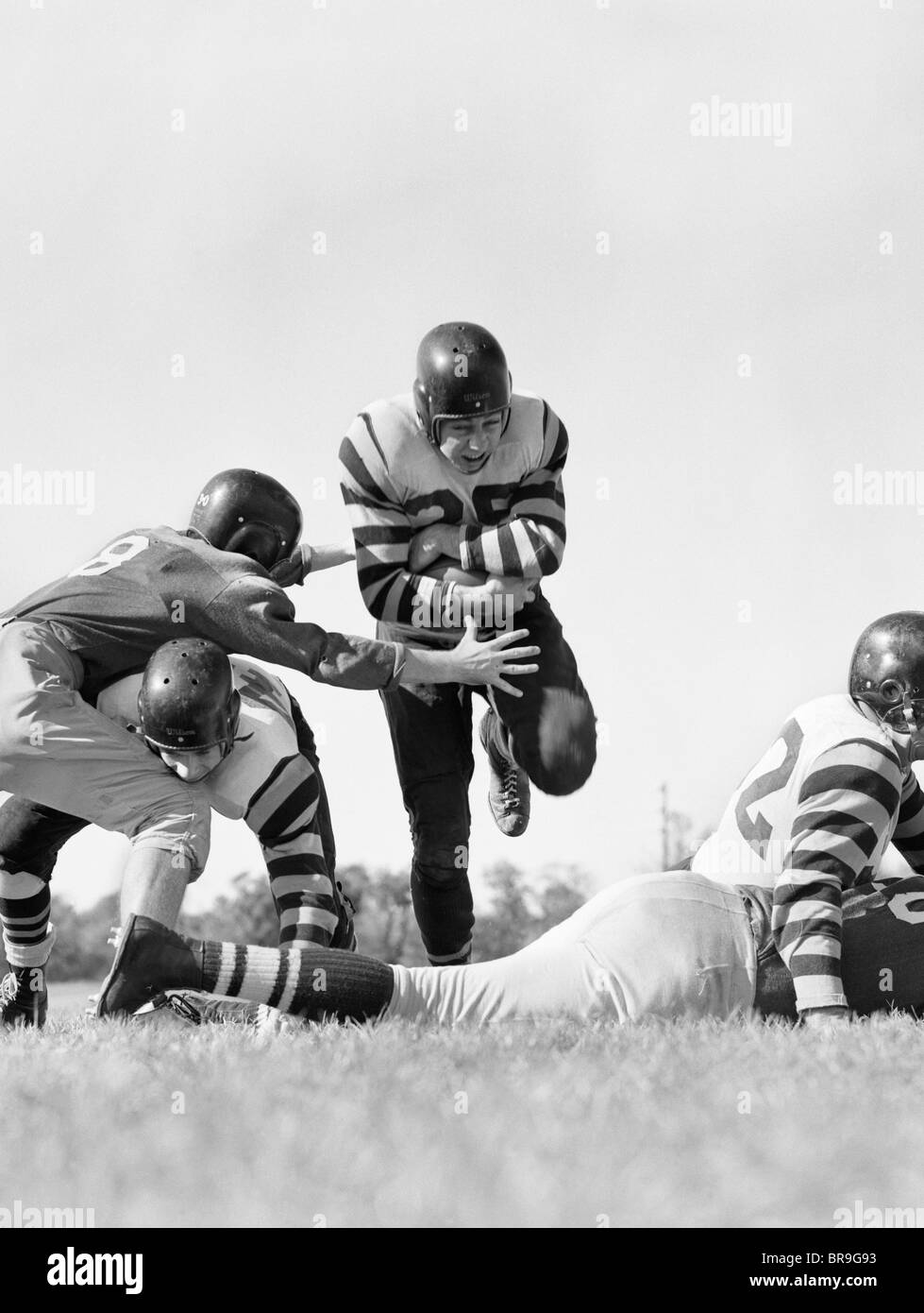 1950s FIVE MEN PLAYING FOOTBALL ONE PLAYER RUNNING HOLDING BALL Stock Photo