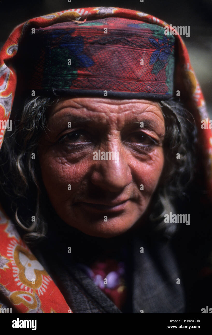 An elderly Wakhi woman in traditional dress sits in her family's winter home in the Little Pamir Wakhan Corridor Stock Photo