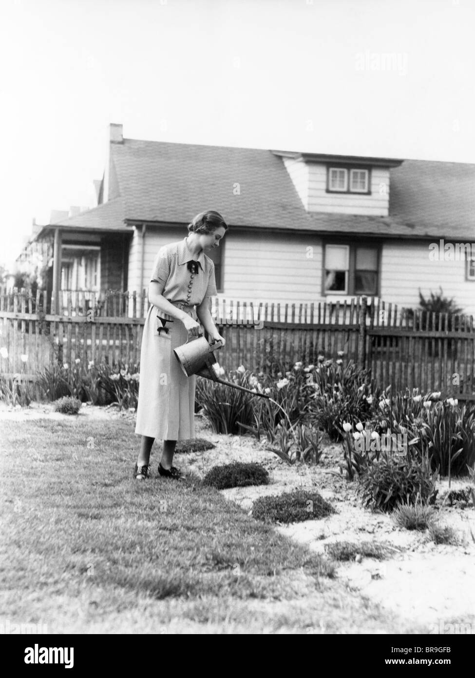 1930s WOMAN WATERING GARDEN  WITH WATER CAN Stock Photo