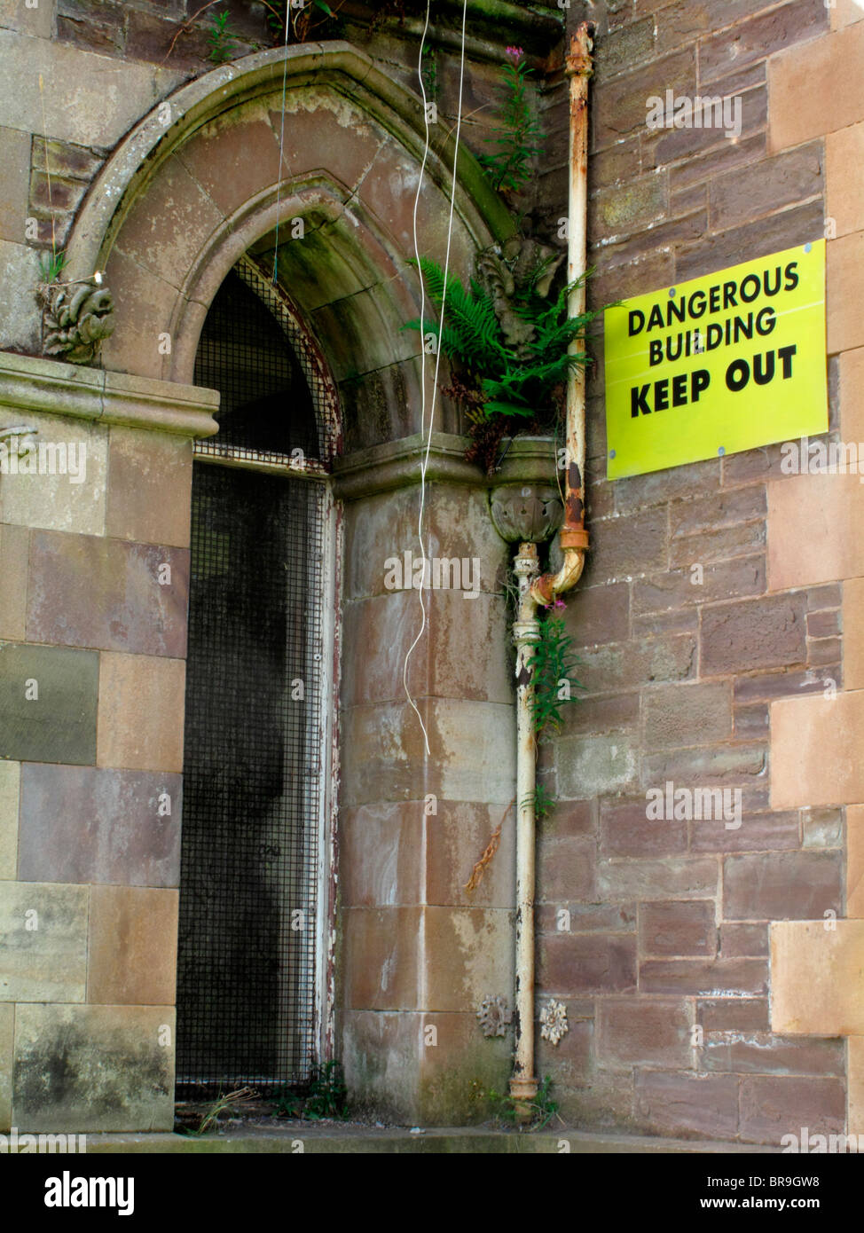 An old decrepit  Victorian building with a yellow sign - 'Dangerous building. Keep out ' stuck to its walls. Stock Photo