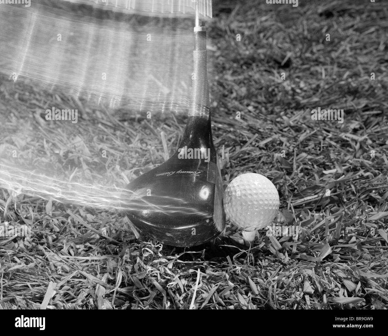 1960s MOVING DRIVER GOLF CLUB HITTING BALL ON TEE IN GRASS Stock Photo