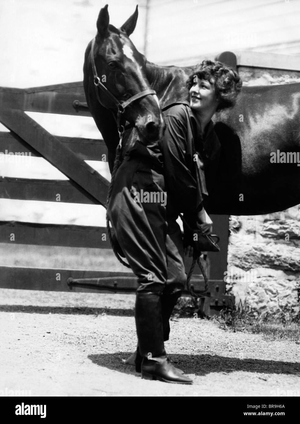 1900s 1910s YOUNG WOMAN WITH UPSWEPT HAIR LIFTING FRONT LEG OF HORSE