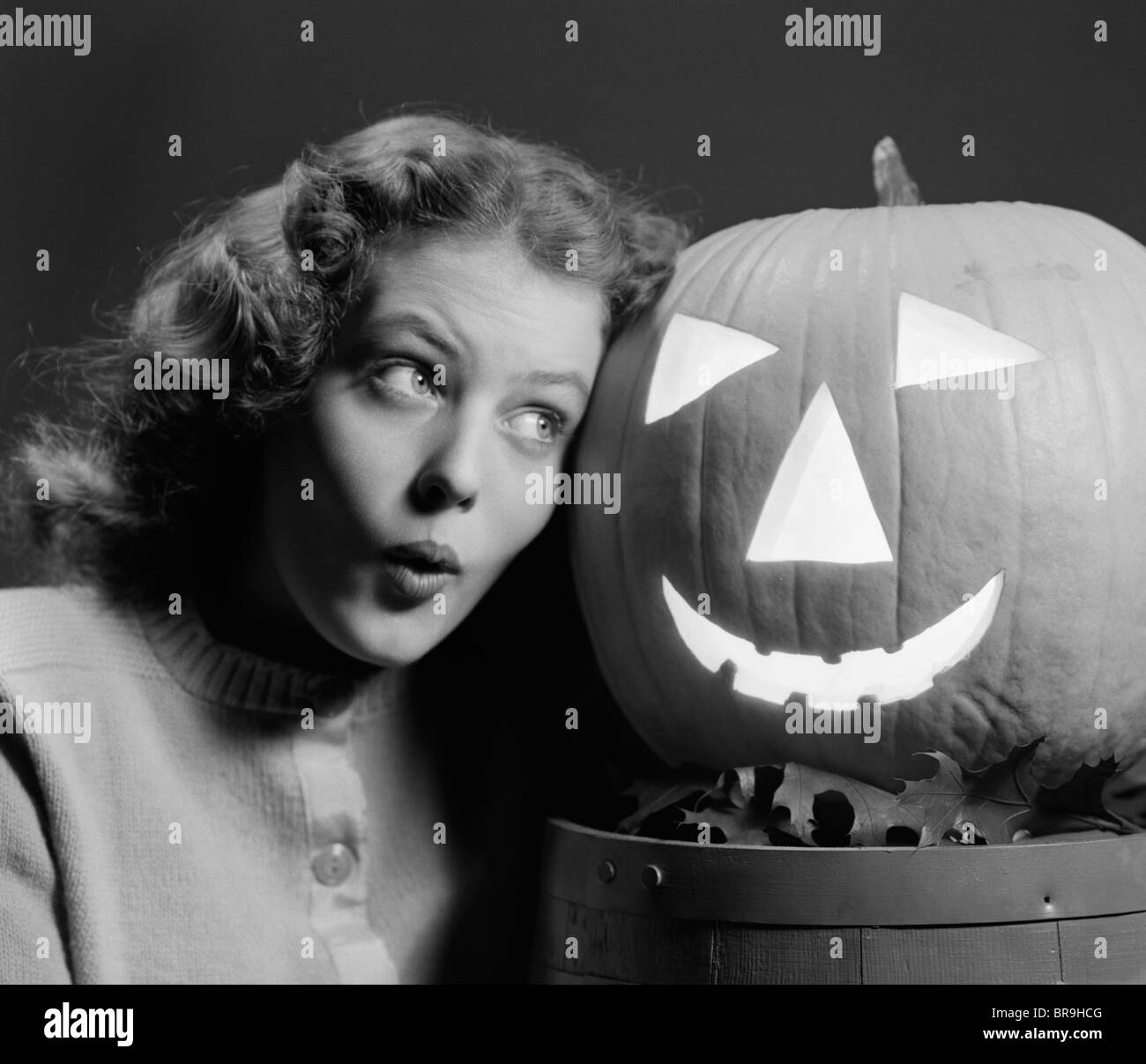 1940s TEEN GIRL WITH SCARED EXPRESSION HEAD TO HEAD WITH CARVED PUMPKIN JACK-O-LANTERN Stock Photo