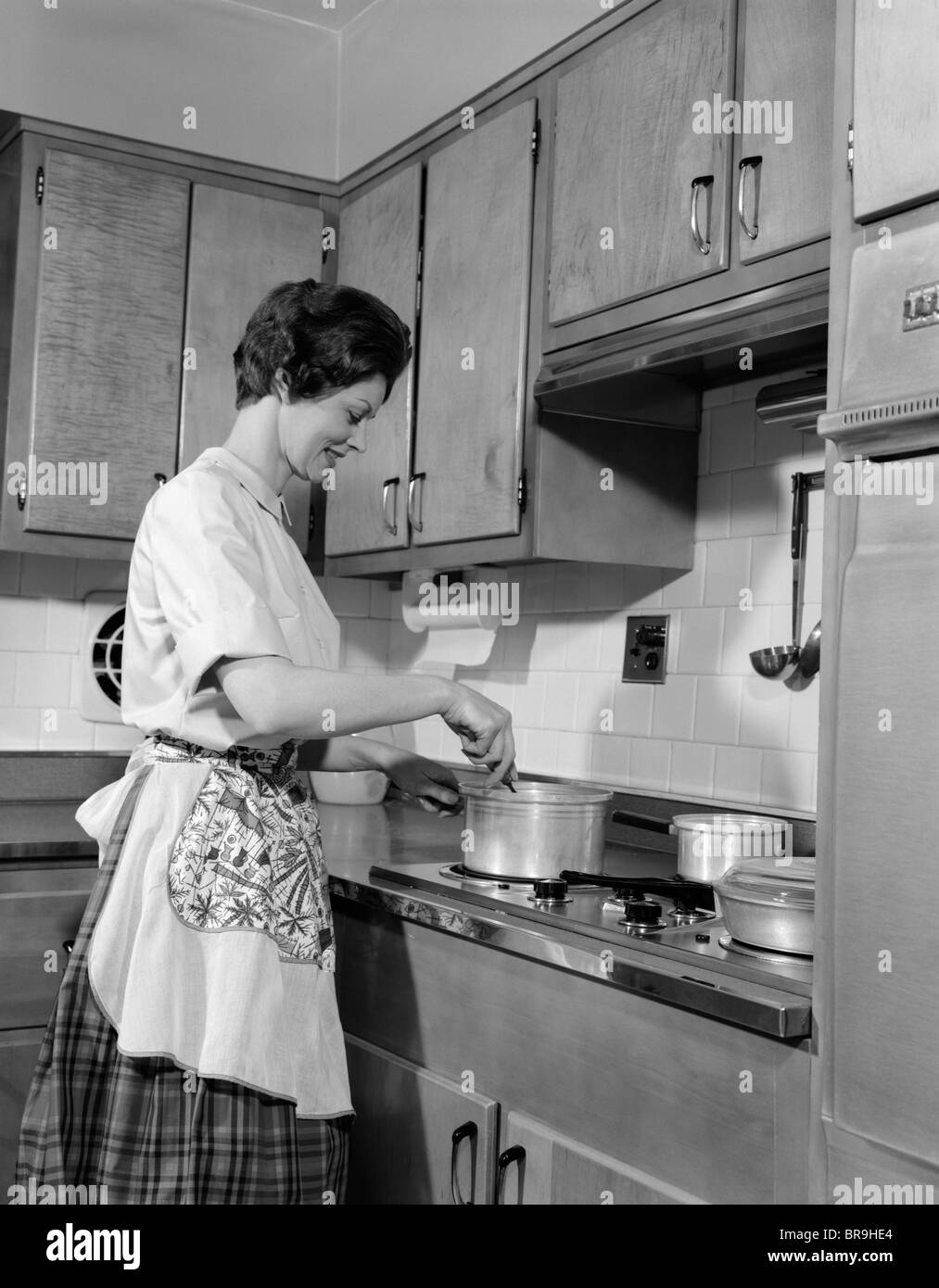 1960s WOMAN KITCHEN COOKING STIRRING POT ON STOVE Stock Photo