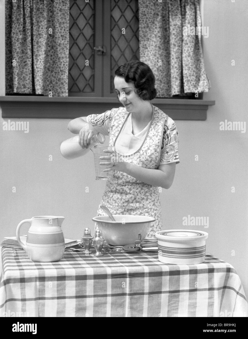 1920s 1930s WOMAN POURING MILK INTO MEASURING CUP Stock Photo