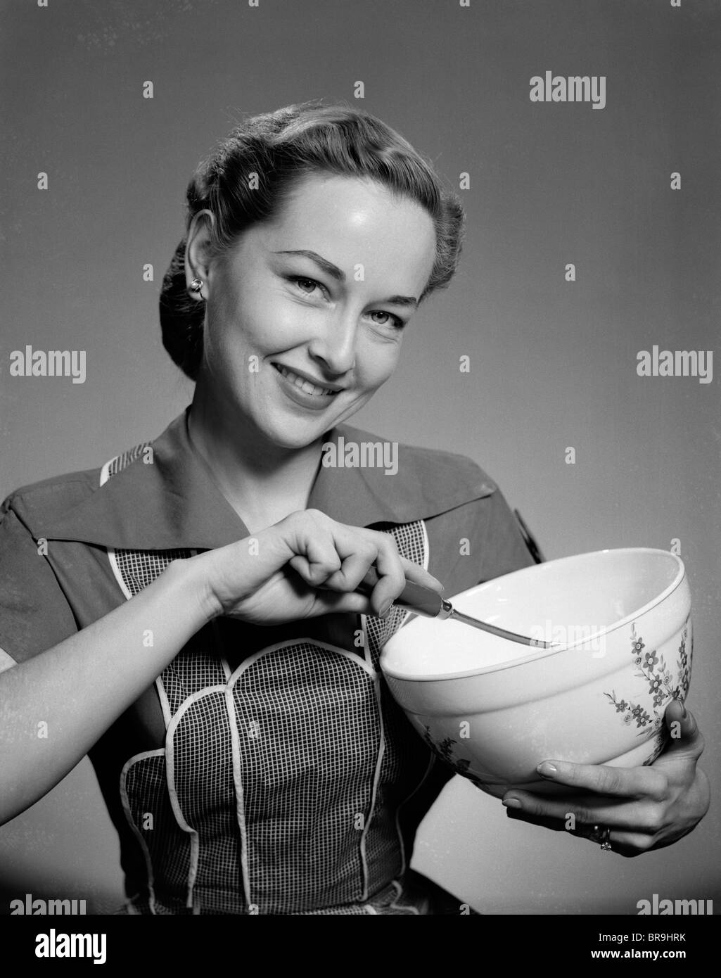 1950s SMILING WOMAN STIRRING MIXING BOWL LOOKING AT CAMERA Stock Photo