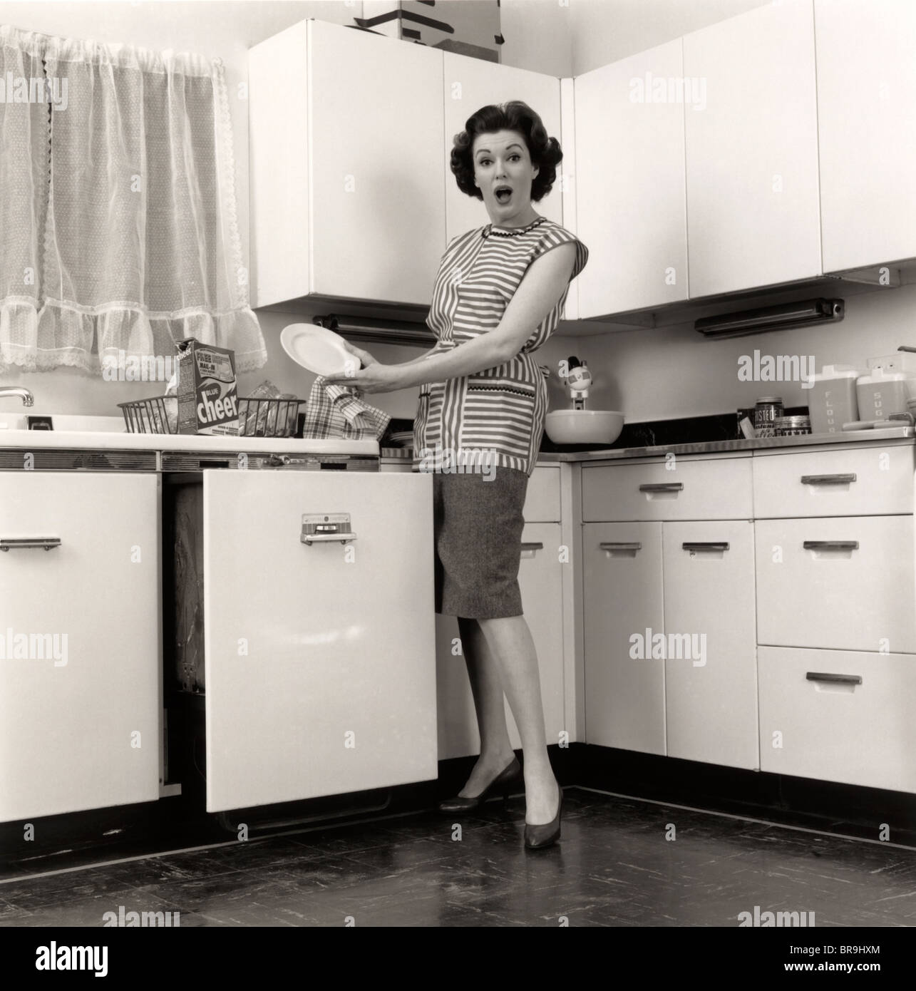 1950s WOMAN HOUSEWIFE WEARING SMOCK PUTTING DISHES IN AUTOMATIC Stock