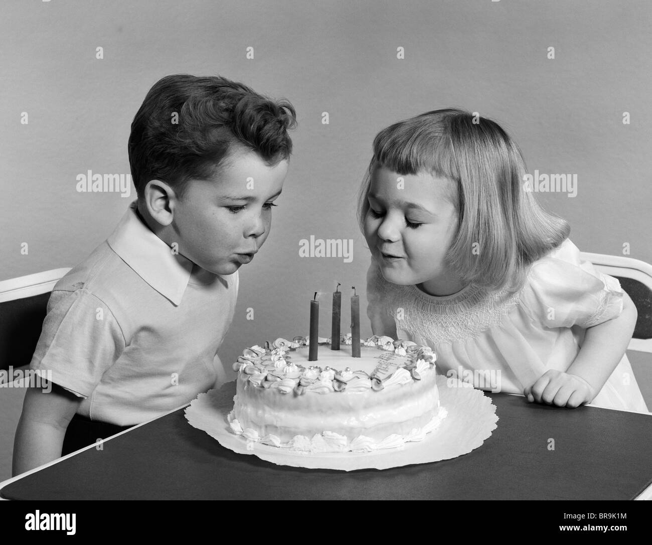 1940s 1950s TWO CHILDREN BLOWING OUT BIRTHDAY CANDLES Stock Photo