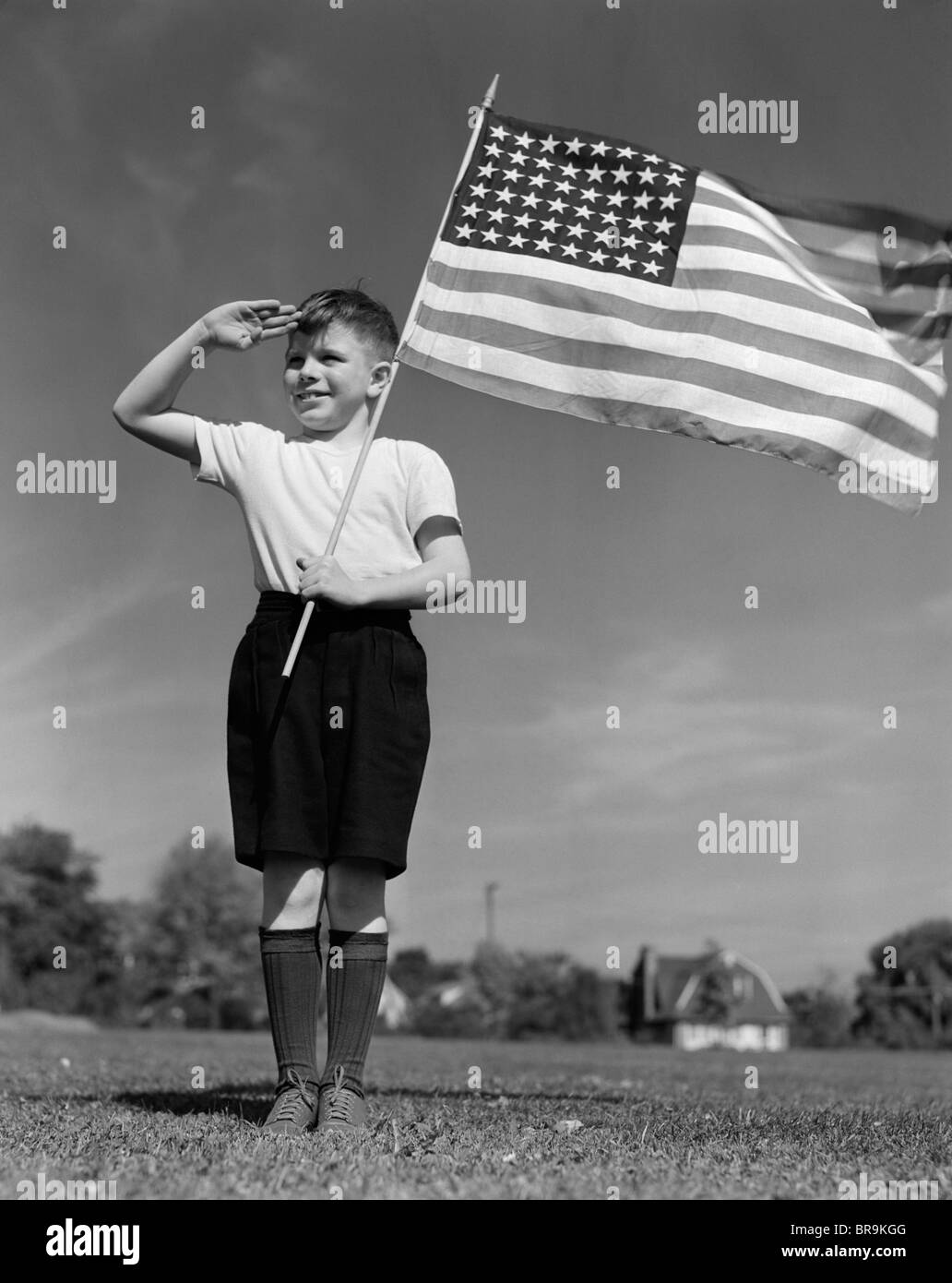 1940s BOY HOLDING AMERICAN FLAG SALUTING WEARING SHORT PANTS Stock Photo