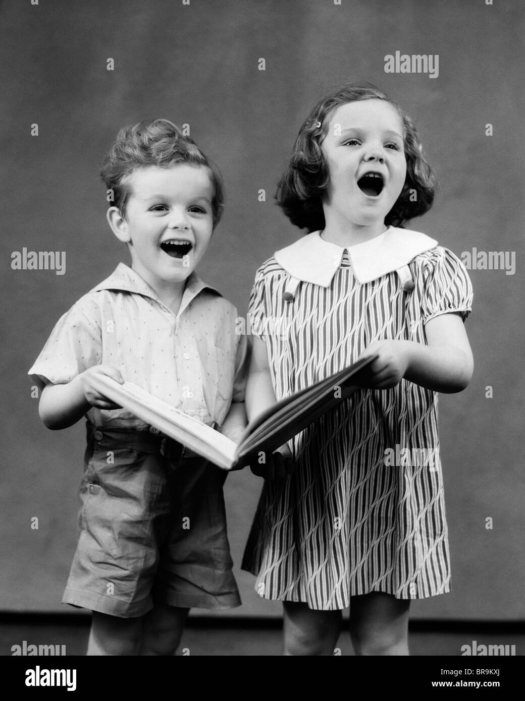 1930s TWO CHILDREN STANDING SINGING Stock Photo