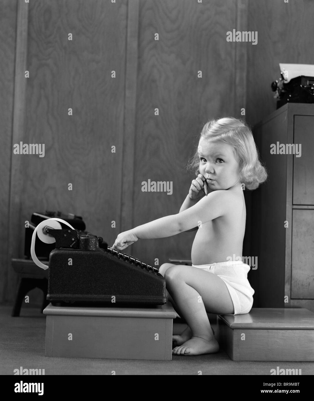 1940s CHILD SITTING TYPING ON ADDING MACHINE FUNNY FACIAL EXPRESSION Stock Photo