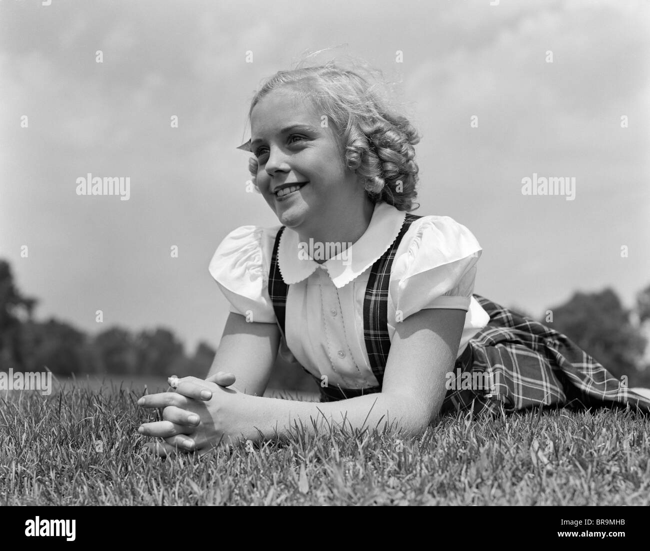 1940s BLOND GIRL SMILING LYING ON GRASS Stock Photo