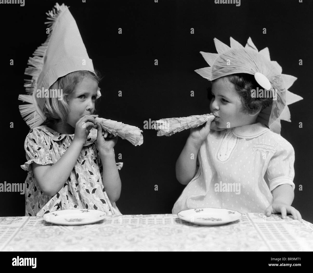 1930s 2 LITTLE GIRLS WITH NOISE MAKERS PARTY HATS Stock Photo