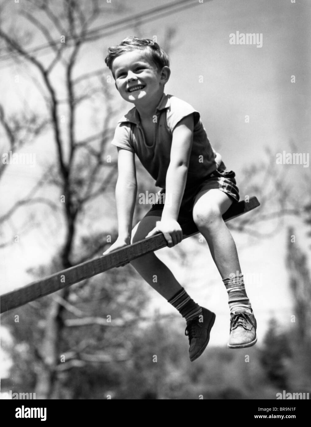 1930s SMILING BOY SITTING ON SEESAW Stock Photo